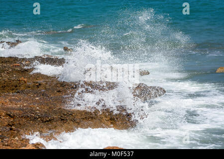 Potenti onde del mare la formazione di schiuma, infrangendosi contro la costa rocciosa Foto Stock