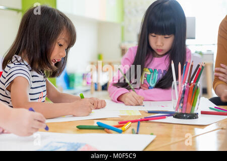 I bambini di età prescolare Disegno con matite colorate su carta bianca sulla tavola in aula con gli amici e il maestro,Kindergarten concetto di istruzione Foto Stock