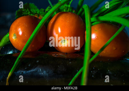 Freschi pomodori rossi con cipolla verde lascia mantenuto su melanzane e gocce di acqua su di essi Foto Stock