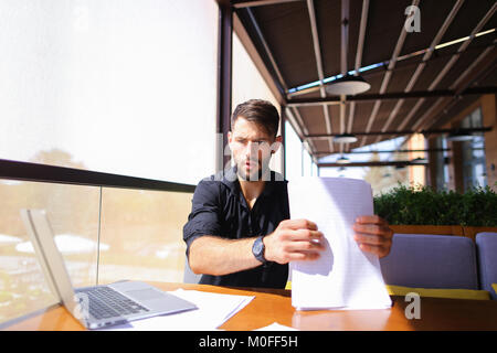 Lavoratore di ufficio ordinamento di carte sul tavolo vicino al computer portatile. Foto Stock