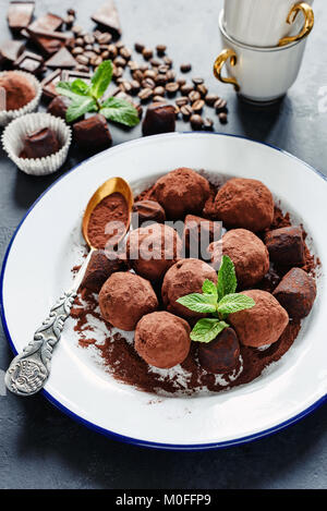 Truffes cioccolato decorate con la menta e la massa di cacao su piastra bianca. Messa a fuoco selettiva, l'immagine verticale Foto Stock
