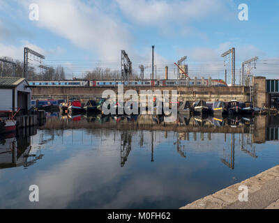 Un treno dalla stazione di St Pancras passa dietro canal barche ormeggiate a St Pancras Lock sul Regents Canal a Londra Foto Stock