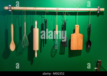 Close up vari utensili da cucina appesi da ferrovia contro il muro verde Foto Stock