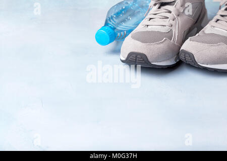 Sneakers grigio e una bottiglia di acqua su uno sfondo blu. Foto Stock