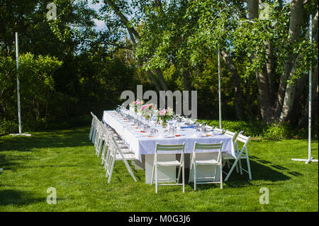 Bianco e lungo matrimonio arte tavolo con sedie in legno, posate, bouquet di fiori, bicchieri, pronto per gli ospiti esterni Foto Stock