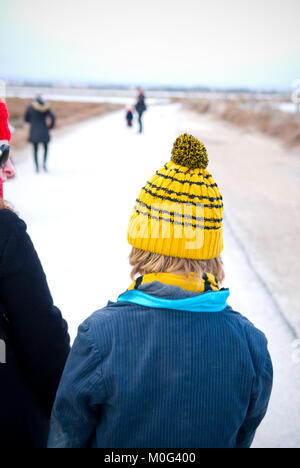 Ripresa posteriore di una madre a spasso il suo figlio con un giallo stripey wooly hat e indossare una tuta pinstriped giacca. A distanza di un padre e figlio attendono Foto Stock