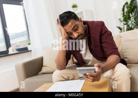 Uomo confuso con documenti e calcolatrice a casa Foto Stock