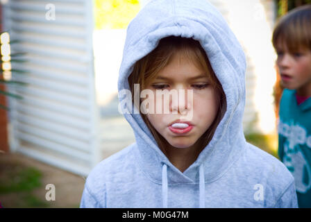Close up di incappucciati ragazza di quattordici anni inizia a soffiare una bolla con il suo bubble gum con la sua 11 anno di età più giovane fratello in background Foto Stock