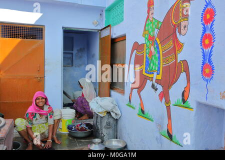 BUNDI, Rajasthan, India - 10 dicembre 2017: sorridere le donne a lavare i panni nel cortile di casa loro con una parete decorata in primo piano Foto Stock