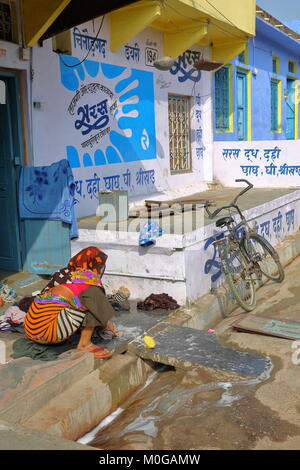 CHITTORGARH, Rajasthan, India - 14 dicembre 2017: scene di strada con una donna con abiti colorati a lavare i panni di fronte alla sua casa Foto Stock