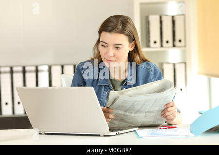 Concentrato intern confrontando news in un computer portatile e il giornale in ufficio Foto Stock