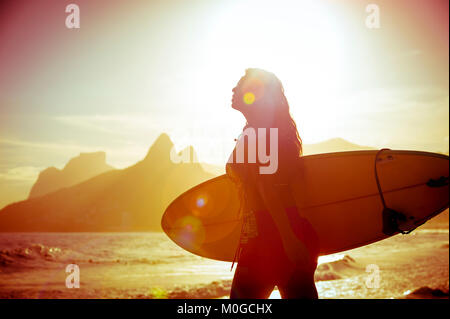 Irriconoscibile silhouette di donna surfer a piedi con la sua tavola da surf a Arpoador, il popolare surf break in Rio de Janeiro, Brasile