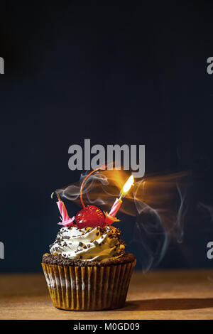 Tortina di compleanno con rosso ciliegia e una candela che brucia nella nuvola di fumo su sfondo scuro Foto Stock