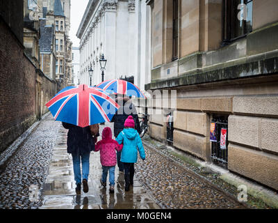 Cambridge turismo - una famiglia a piedi attraverso il centro storico di Cambridge in un giorno di pioggia con Unione Jack ombrelloni Foto Stock