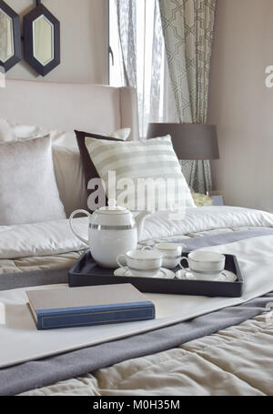 Vassoio decorativo con libro e set per il tè sul letto in camera da letto moderna Foto Stock