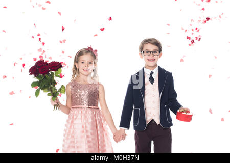 Bella elegante kids con rose e a forma di cuore scatola regalo tenendo le mani e sorridendo in telecamera su bianco Foto Stock