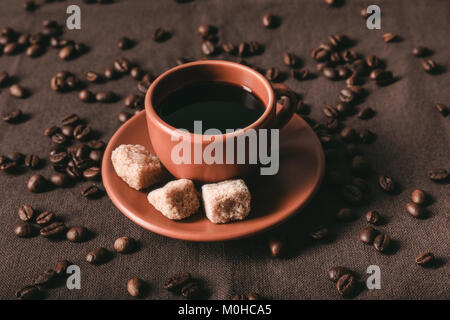 Ceramica tazza di caffè con zucchero di canna cubi e dispersi i grani di caffè sul panno marrone Foto Stock