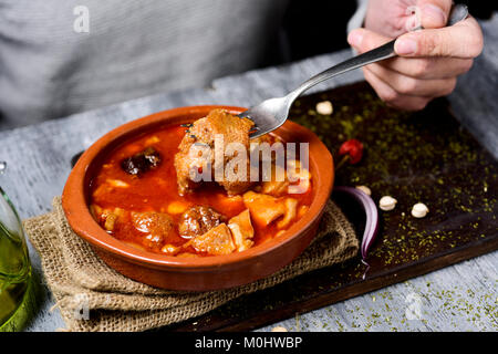 Primo piano di un giovane uomo caucasico avente una porzione di spagnolo callos, un tipico stufato di trippa di manzo e ceci, da un recipiente di terracotta collocati su Foto Stock