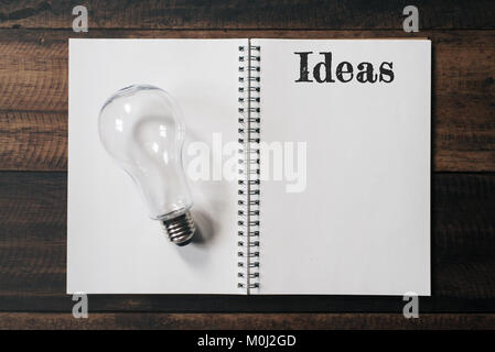 La lampadina e il notebook con idee parola su un tavolo di legno. idee concetto Foto Stock