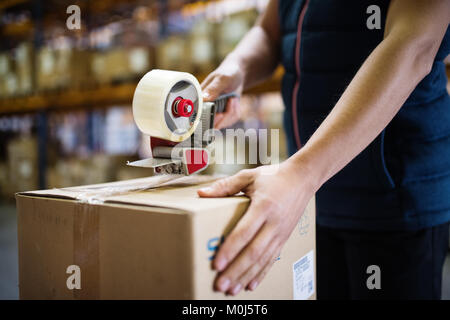 Magazzino maschio lavoratore la sigillatura di scatole di cartone. Foto Stock