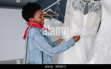Sorridente donna africana shopping per matrimonio abito nuziale in boutique. La scelta della sposa abito bianco al negozio di moda nuziale. Foto Stock