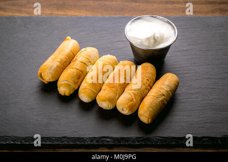 Tequeños, tipici snack venezuelano con salsa di aglio su una pietra nera dello sfondo. Foto Stock