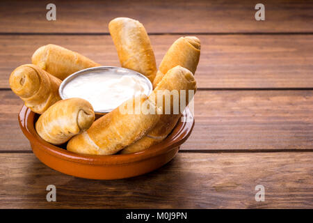Tequeños, tipici snack venezuelano con salsa di aglio su uno sfondo di legno Foto Stock