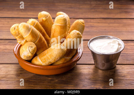 Tequeños, tipici snack venezuelano con salsa di aglio su uno sfondo di legno Foto Stock