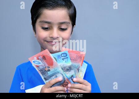 Allegro kid holding denaro. Dollari australiani in mani del bambino felice. Concetto di pocket money. Emozionato bambino con denaro. Foto Stock