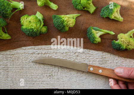 Vista superiore della donna mani di taglio broccoli verdi sul tavolo di legno. Mangiare sano concetto Foto Stock