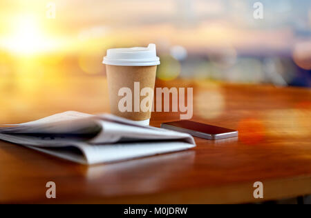 Tazza da caffè, smartphone e giornale sul tavolo Foto Stock