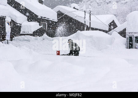 Un uomo è la cancellazione di una strada dalla neve in un villaggio alpino Foto Stock