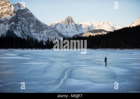 La figura in piedi da solo su un lago ghiacciato nelle montagne rocciose. In alto lago Kananaskis, Alberta. Foto Stock