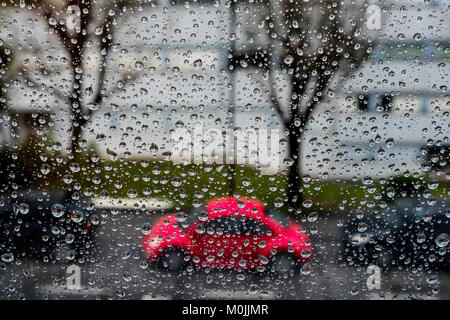 Auto rossa è vedere dietro le gocce di pioggia in un vetro di un finestrino Foto Stock