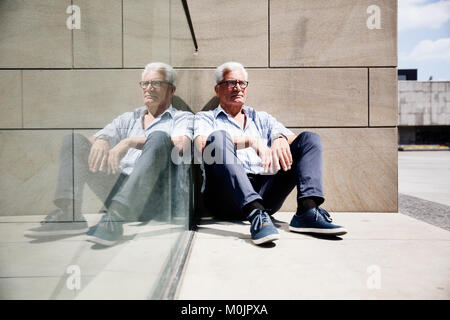 Grey-haired senior sul pavimento di fronte a un muro e si riflette in una lastra di vetro, Colonia, nella Renania settentrionale-Vestfalia, Germania Foto Stock
