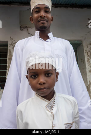 Kid indossando vestiti tradizionali & kufi per il mawlid festival, celebrando con suo padre, l'isola di Lamu, Kenya Foto Stock