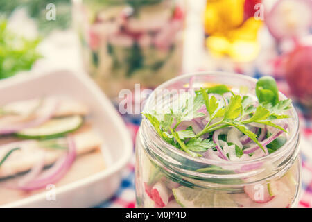 In casa insalate sane con verdure, cipolla, prezzemolo e lattuga in vaso. Tagliate a fette i filetti di aringhe, tagliare la cipolla e il calcare sulla piastra bianca. Tonificazione. Selet Foto Stock