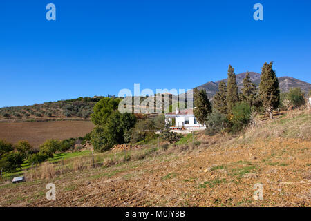 Un allevamento bianco villa sul pendio di una collina con ulivi e terreno coltivato nei pressi del paesaggio di montagna sotto un cielo blu in Andalusia Spagna Foto Stock