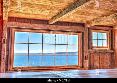 Guardando attraverso la vecchia finestra di casa con scogliera e vista oceano nella isola di Bonaventura, Quebec, Canada, acqua azzurra Foto Stock