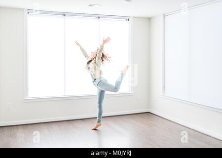 Una giovane donna felice il salto nel vuoto nuove e moderne camere con pavimenti in legno e grandi finestre soleggiate in appartamento Foto Stock