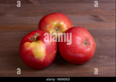 Tre mele rosse giacciono su una tavola di legno Foto Stock