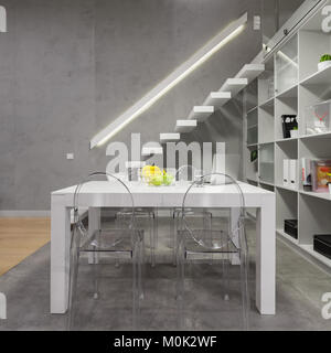 Appartamento Loft con tavolo bianco, moderne sedie trasparenti, scale e della libreria Foto Stock