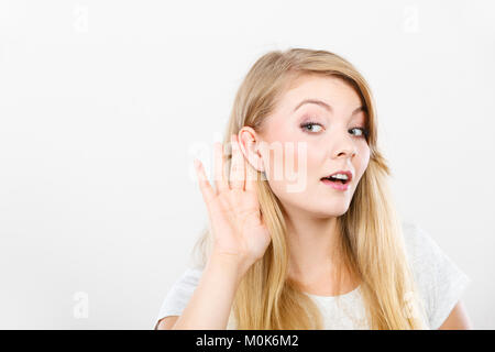 Gossip,indiscrezioni, sussurro, audizione del concetto. Giovane donna bionda mettere mano orecchio per ascoltare meglio. Studio shot su sfondo bianco. Foto Stock