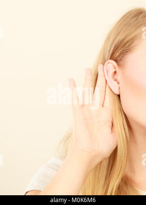 Gossip,indiscrezioni, sussurro, audizione del concetto. Giovane donna bionda mettere mano orecchio per ascoltare meglio. Studio shot su sfondo bianco. Foto Stock