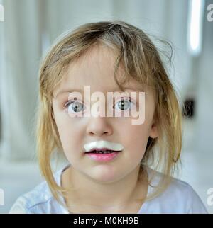 Close up divertente ritratto di carino bambina con latte baffi. Ritratto di un po' di felice ragazza con yogurt sulla faccia. Foto Stock