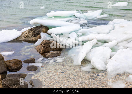 Litorale con pezzi di ghiaccio congelato, conchiglie, rocce e acqua salata Foto Stock