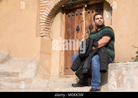 Giovane uomo seduto di fronte decorata porta di legno, villaggio Masuleh Foto Stock