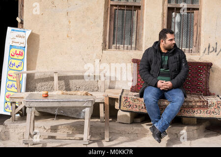 Giovane uomo seduto sul tappeto persiano di fronte teahouse parete di argilla, villaggio Masuleh Foto Stock