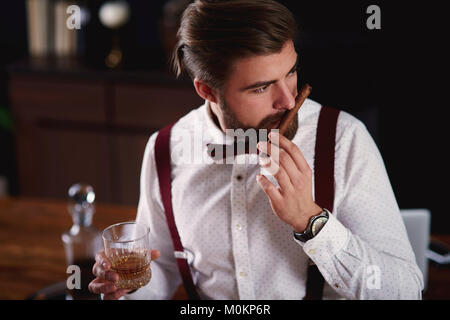 Imprenditore con un bicchiere di whiskey e sigari cubani in ufficio Foto Stock