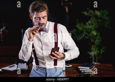 Uomo bello di fumare sigari cubani e la lettura di un messaggio di testo Foto Stock